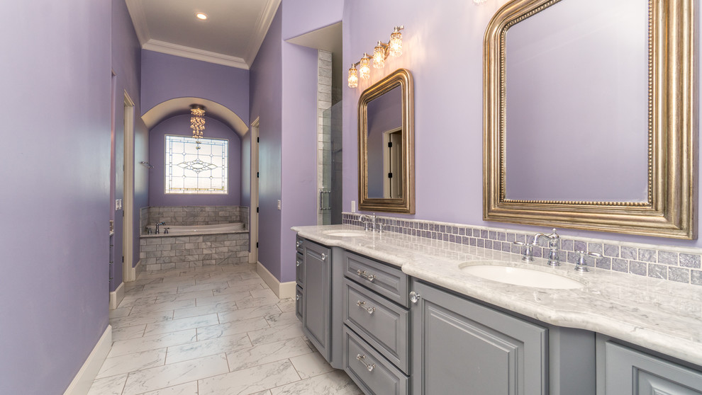 Large traditional master bathroom in Phoenix with raised-panel cabinets, grey cabinets, a drop-in tub, an alcove shower, gray tile, stone tile, purple walls, marble floors, an undermount sink, marble benchtops, grey floor and a hinged shower door.