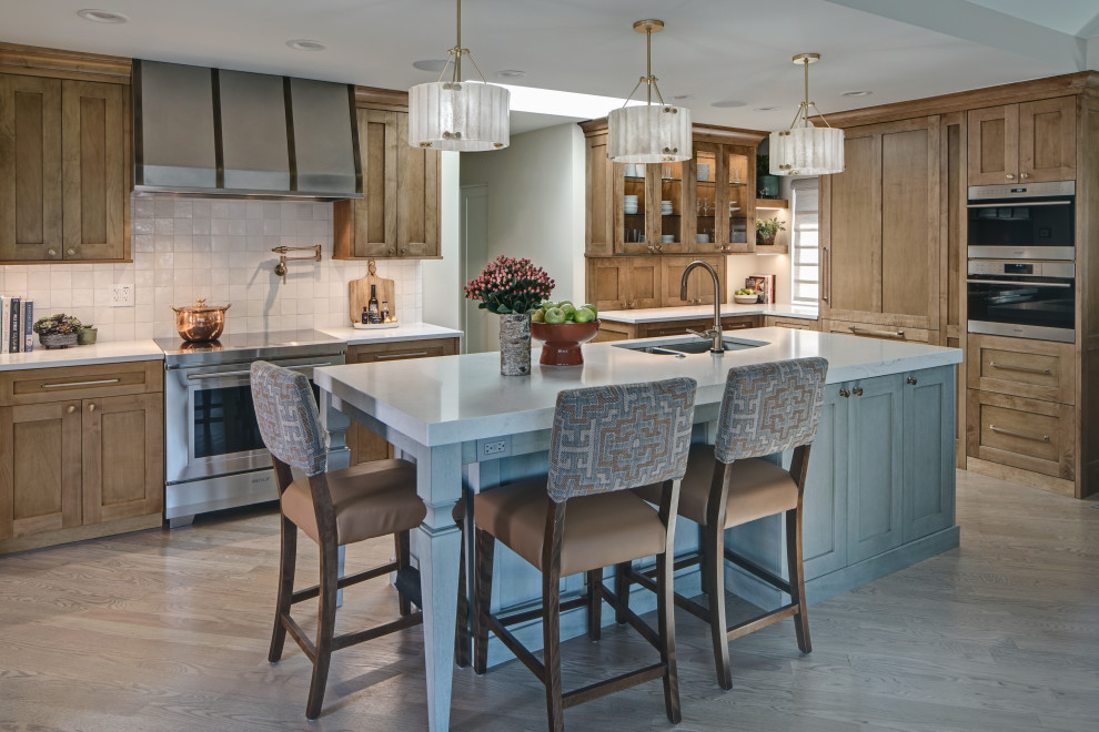 Photo of a mid-sized transitional l-shaped kitchen in Chicago with an undermount sink, shaker cabinets, medium wood cabinets, quartz benchtops, white splashback, ceramic splashback, stainless steel appliances, medium hardwood floors, with island, brown floor and white benchtop.