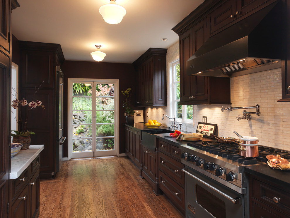 Inspiration for a traditional galley separate kitchen in San Francisco with soapstone benchtops, stainless steel appliances, recessed-panel cabinets, dark wood cabinets, white splashback, an integrated sink, medium hardwood floors and brown floor.
