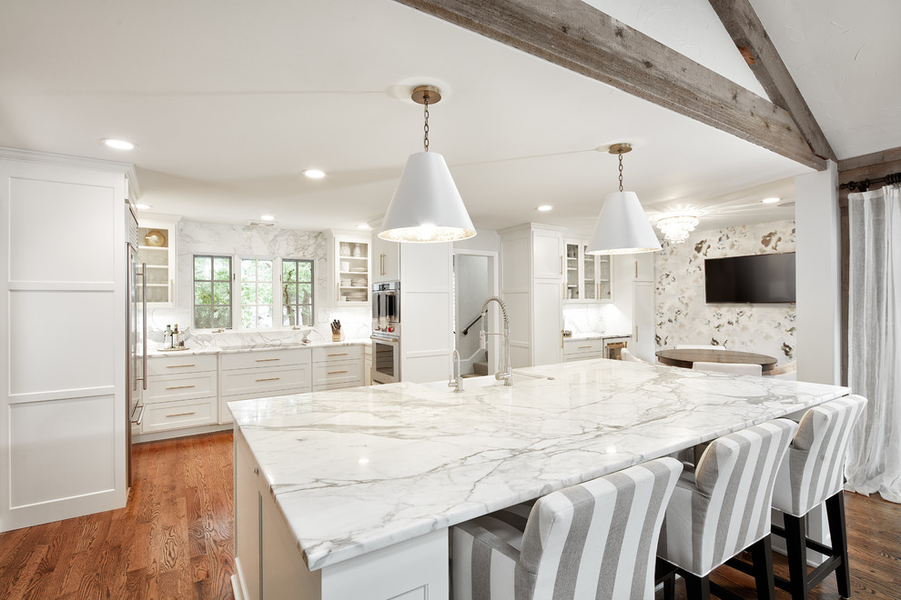 Example of a large transitional u-shaped medium tone wood floor and brown floor eat-in kitchen design with a farmhouse sink, shaker cabinets, white cabinets, marble countertops, white backsplash, marble backsplash, stainless steel appliances and an island