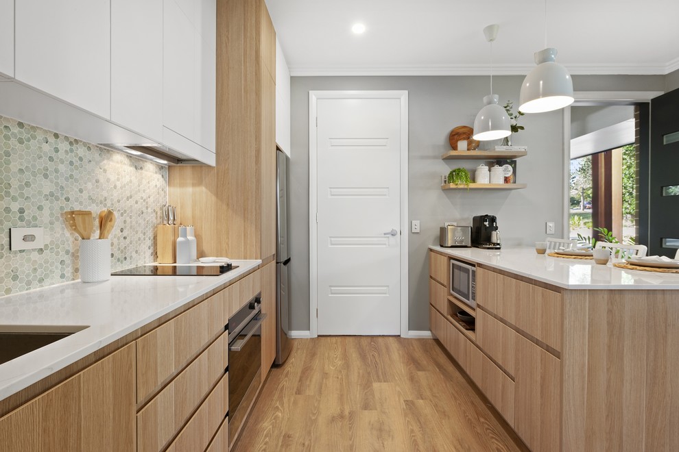 Photo of a small scandinavian galley open plan kitchen in Sydney with an undermount sink, flat-panel cabinets, light wood cabinets, quartz benchtops, green splashback, marble splashback, stainless steel appliances, vinyl floors, with island, beige floor and white benchtop.