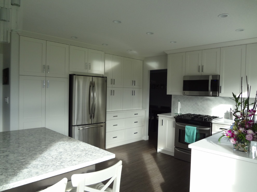 Small transitional l-shaped laminate floor and gray floor home design photo with an undermount sink, shaker cabinets, white cabinets, quartz countertops, multicolored backsplash, marble backsplash, stainless steel appliances, an island and multicolored countertops