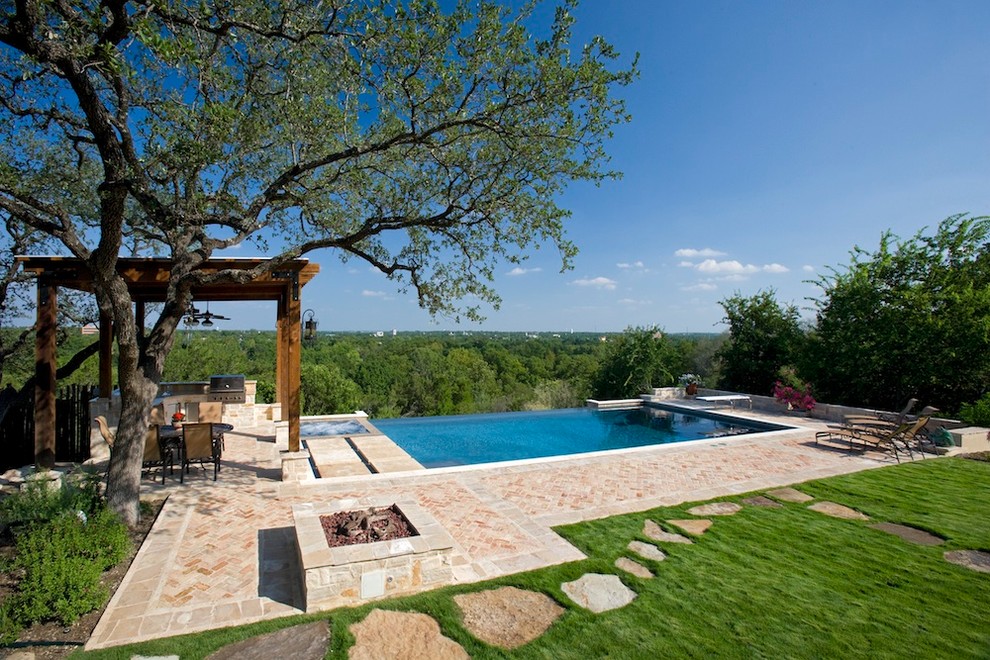 This is an example of a mid-sized traditional backyard rectangular infinity pool in Austin with a hot tub and brick pavers.