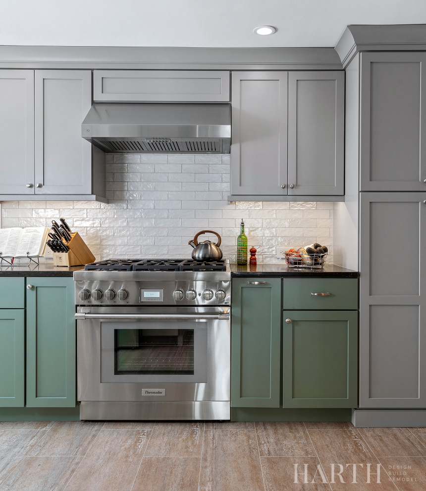 Inspiration for a mid-sized transitional galley separate kitchen in Philadelphia with an undermount sink, shaker cabinets, green cabinets, quartz benchtops, white splashback, porcelain splashback, stainless steel appliances, laminate floors, a peninsula, brown floor and black benchtop.