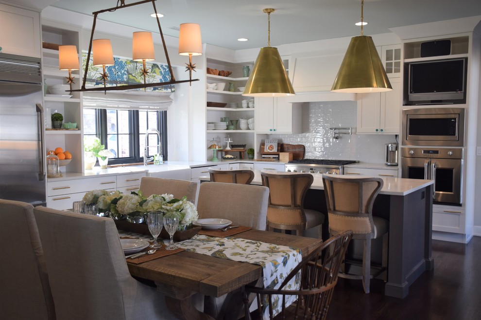 Example of a large transitional dark wood floor eat-in kitchen design with a farmhouse sink, shaker cabinets, white cabinets, quartzite countertops, white backsplash, subway tile backsplash, stainless steel appliances and an island