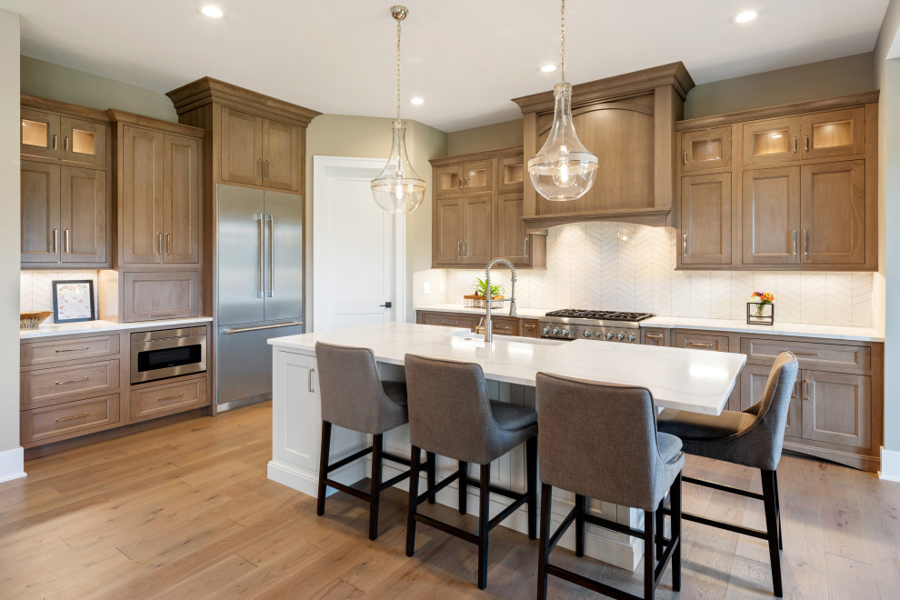 Eat-in kitchen - mid-sized transitional l-shaped medium tone wood floor and gray floor eat-in kitchen idea in Cincinnati with a farmhouse sink, recessed-panel cabinets, medium tone wood cabinets, quartz countertops, white backsplash, ceramic backsplash, stainless steel appliances, an island and white countertops
