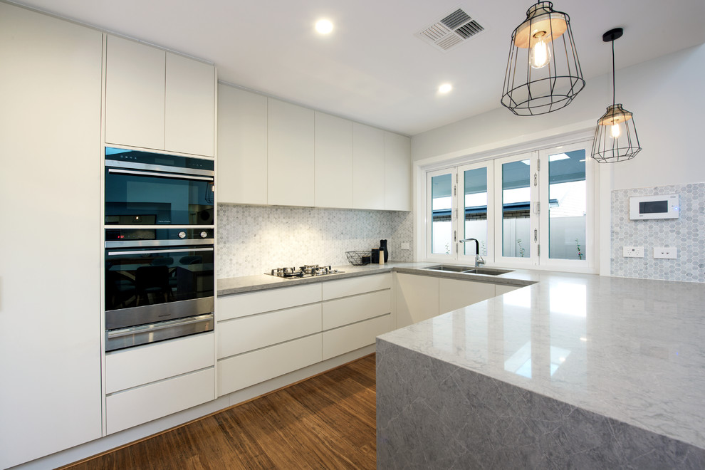 Design ideas for a mid-sized modern u-shaped open plan kitchen in Central Coast with an undermount sink, grey splashback, ceramic splashback, black appliances, bamboo floors, brown floor, flat-panel cabinets, solid surface benchtops and no island.