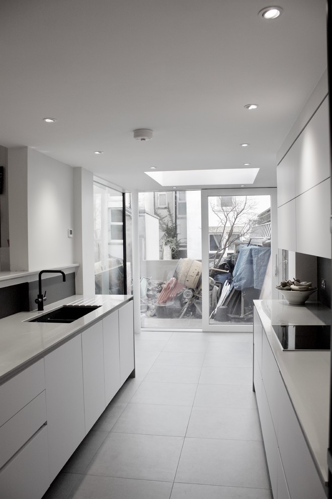 This is an example of a large modern galley kitchen/diner in Other with a built-in sink, flat-panel cabinets, white cabinets, composite countertops, grey splashback, glass sheet splashback, black appliances, ceramic flooring and a breakfast bar.
