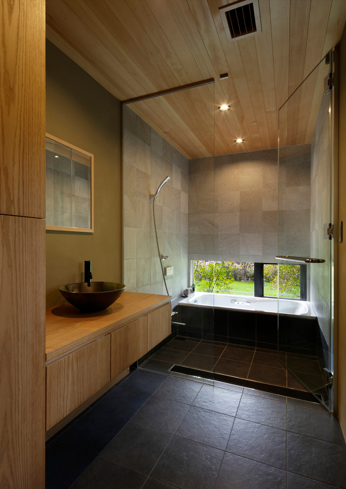 Contemporary bathroom in Other with flat-panel cabinets, a corner tub, an open shower, multi-coloured walls, a vessel sink, wood benchtops, black floor and an open shower.