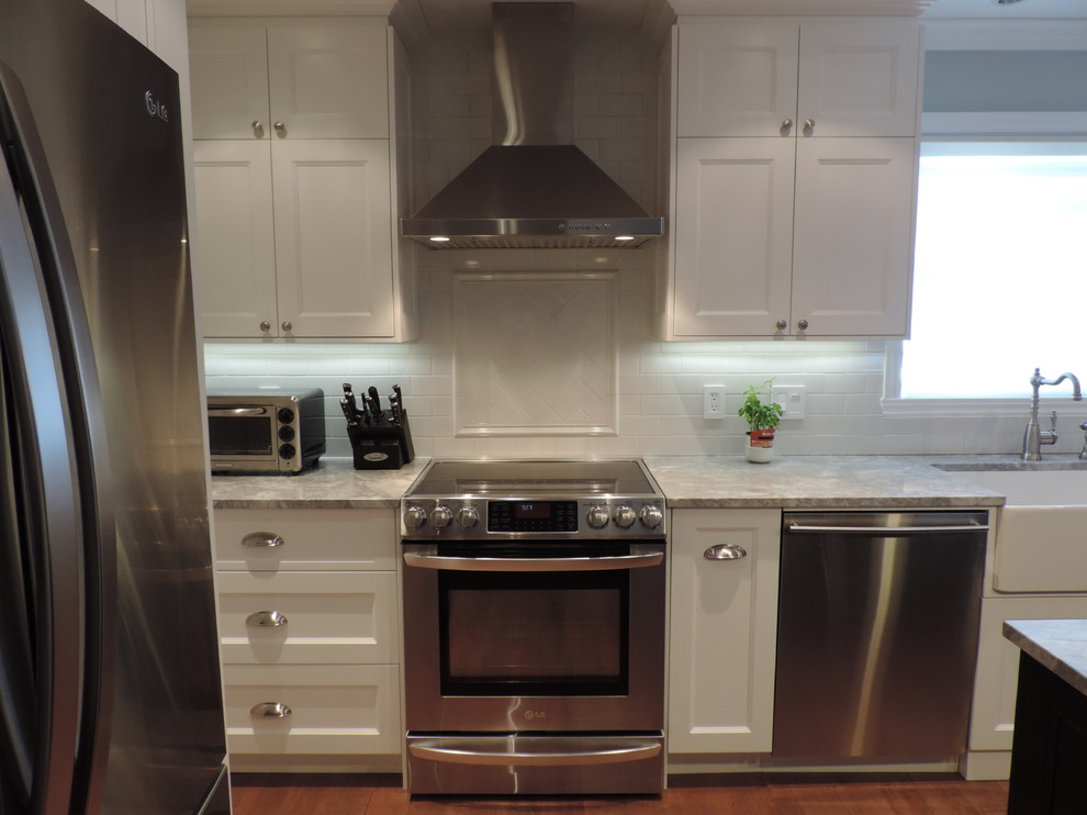 Mid-sized transitional l-shaped eat-in kitchen in Montreal with a farmhouse sink, shaker cabinets, white cabinets, granite benchtops, white splashback, ceramic splashback, stainless steel appliances, light hardwood floors and with island.