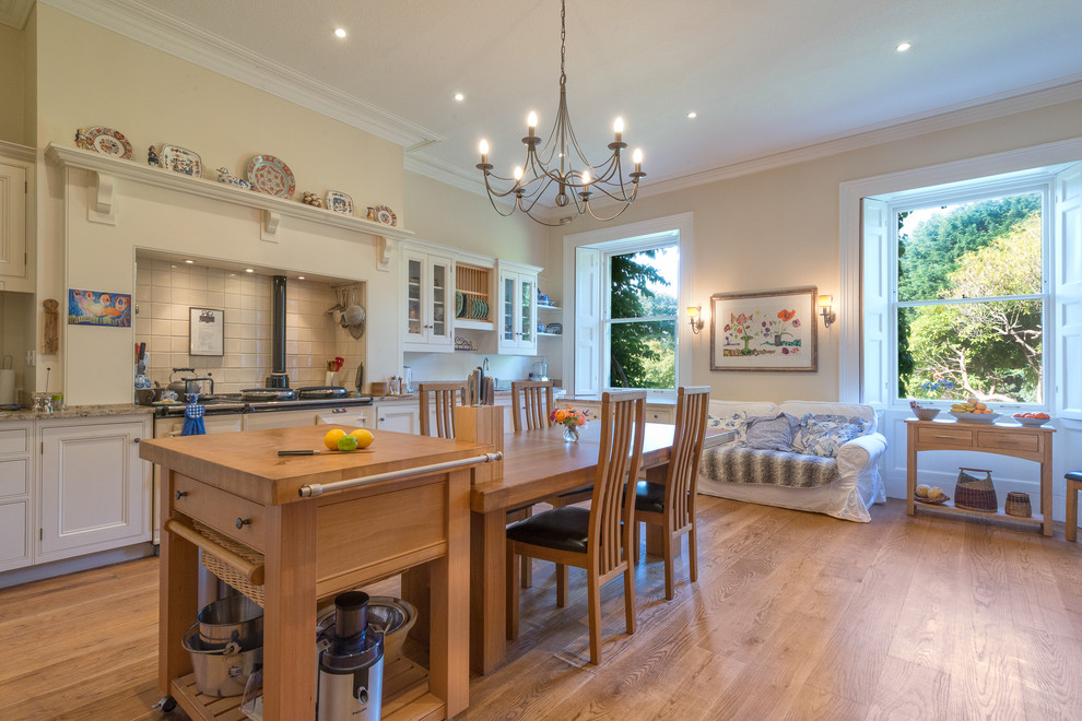 Inspiration for an expansive country l-shaped eat-in kitchen in Devon with an undermount sink, recessed-panel cabinets, white cabinets, white splashback, ceramic splashback, medium hardwood floors, with island and white appliances.