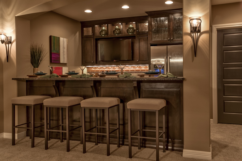 This is an example of a mid-sized country single-wall seated home bar in Omaha with raised-panel cabinets, dark wood cabinets, granite benchtops, brown splashback, ceramic splashback, carpet and brown floor.