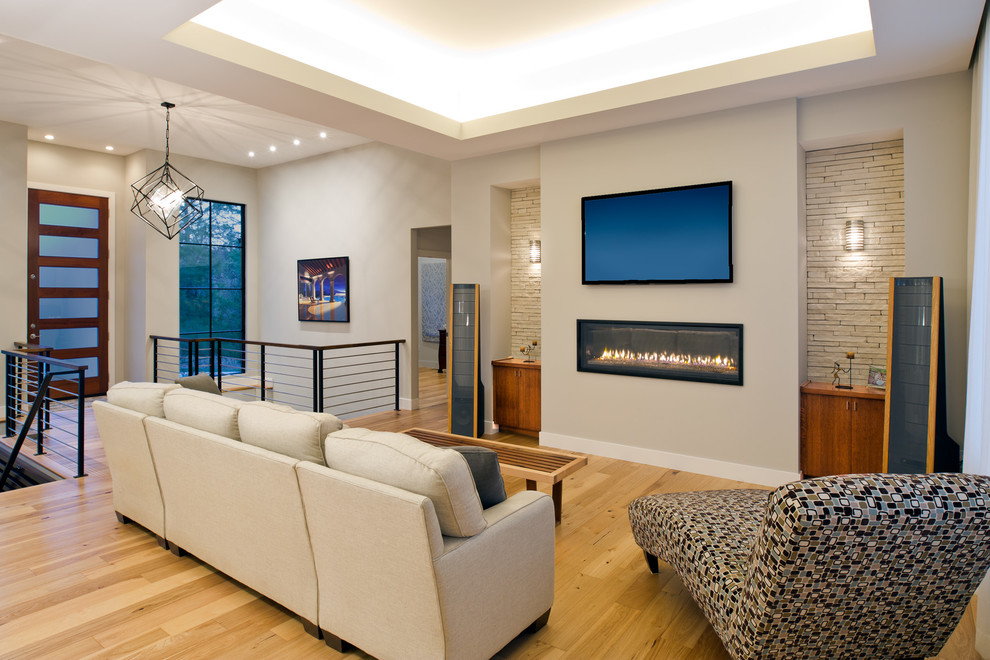 Photo of a transitional living room in Other with beige walls, light hardwood floors, a standard fireplace, a wall-mounted tv and brown floor.