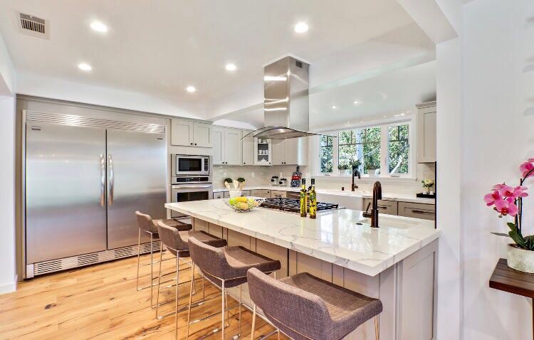 Photo of a large transitional l-shaped eat-in kitchen in Los Angeles with a farmhouse sink, shaker cabinets, grey cabinets, marble benchtops, white splashback, stainless steel appliances, light hardwood floors, with island, beige floor, ceramic splashback and white benchtop.