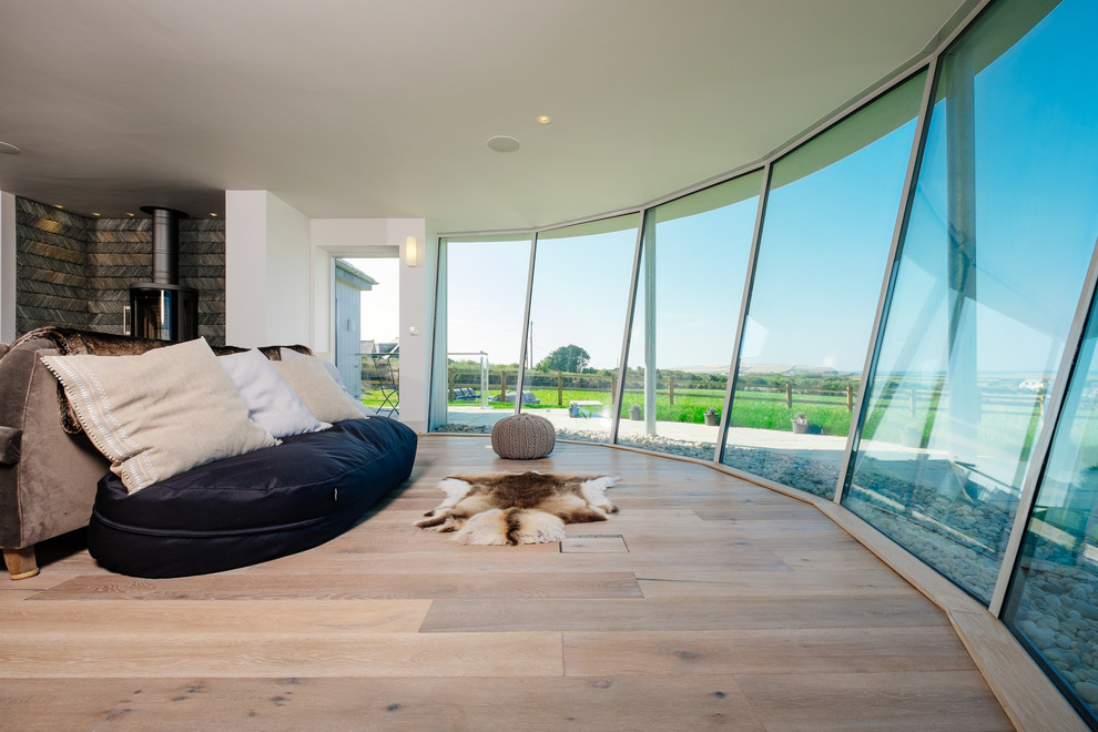 This is an example of a contemporary master bedroom in Cornwall with white walls, light hardwood floors and a wood stove.