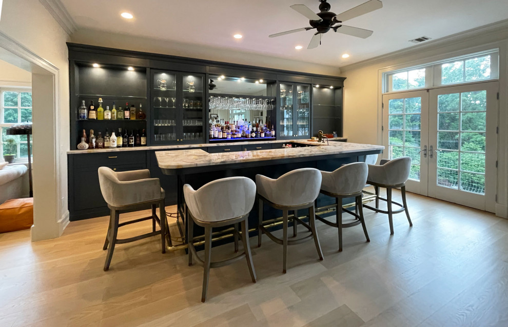 This is an example of a large transitional single-wall seated home bar in New York with an integrated sink, shaker cabinets, black cabinets, quartz benchtops, blue splashback, engineered quartz splashback, light hardwood floors, brown floor and blue benchtop.