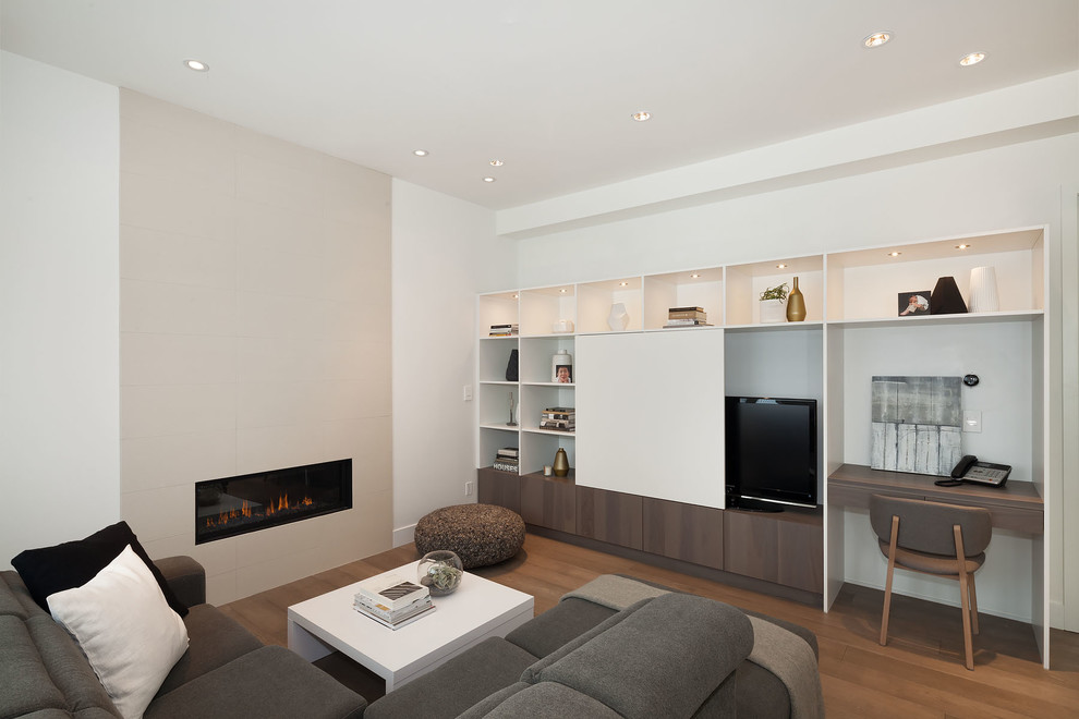 This is an example of a large modern family room in Vancouver with white walls, medium hardwood floors, no fireplace, a tile fireplace surround and a freestanding tv.