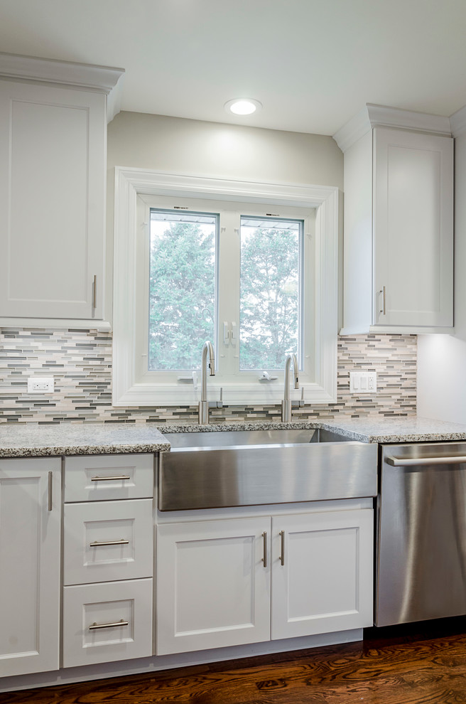 Mid-sized transitional u-shaped medium tone wood floor eat-in kitchen photo in Chicago with a farmhouse sink, recessed-panel cabinets, white cabinets, granite countertops, gray backsplash, glass tile backsplash, stainless steel appliances and an island