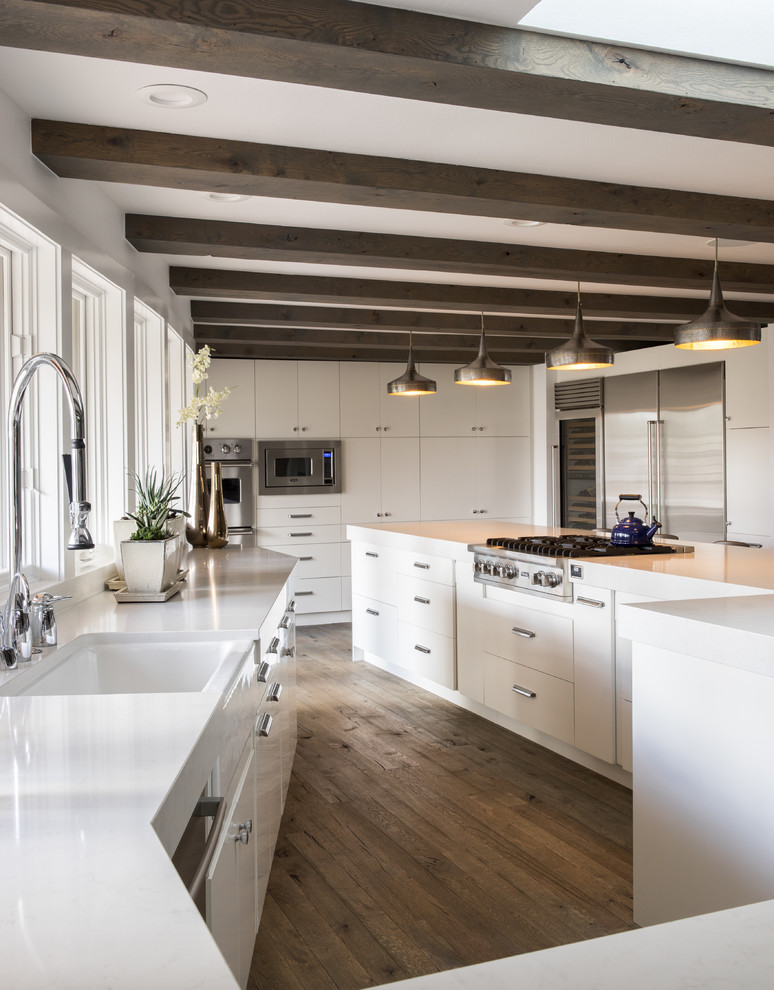 Photo of a large contemporary u-shaped separate kitchen in Denver with a farmhouse sink, flat-panel cabinets, white cabinets, stainless steel appliances, medium hardwood floors, with island, white splashback, beige floor and white benchtop.