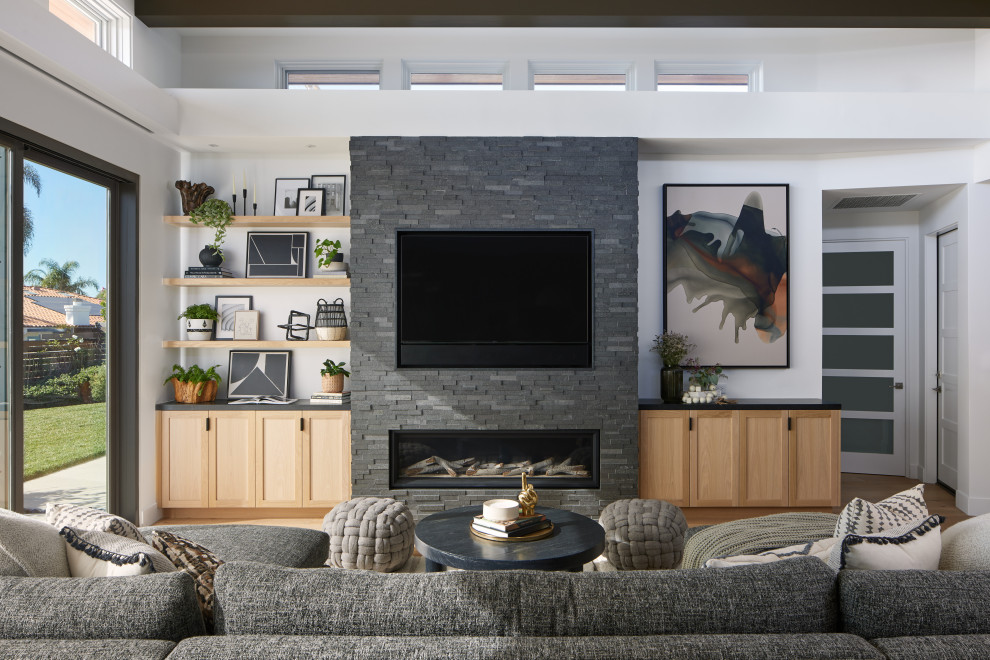 ロサンゼルスにあるトランジショナルスタイルのおしゃれなLDK (白い壁、淡色無垢フローリング、積石の暖炉まわり、ベージュの床、表し梁、横長型暖炉、壁掛け型テレビ) の写真