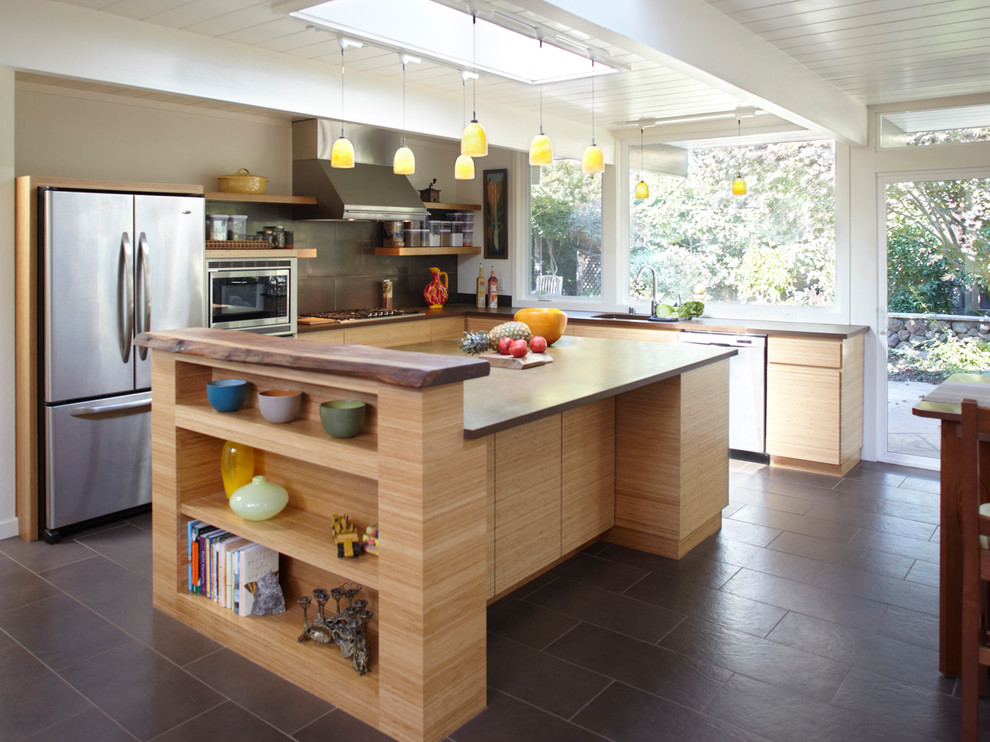 Mid-sized midcentury l-shaped kitchen in San Francisco with flat-panel cabinets, light wood cabinets, grey splashback, stainless steel appliances, an undermount sink, wood benchtops, stone slab splashback, porcelain floors, with island, black floor and brown benchtop.