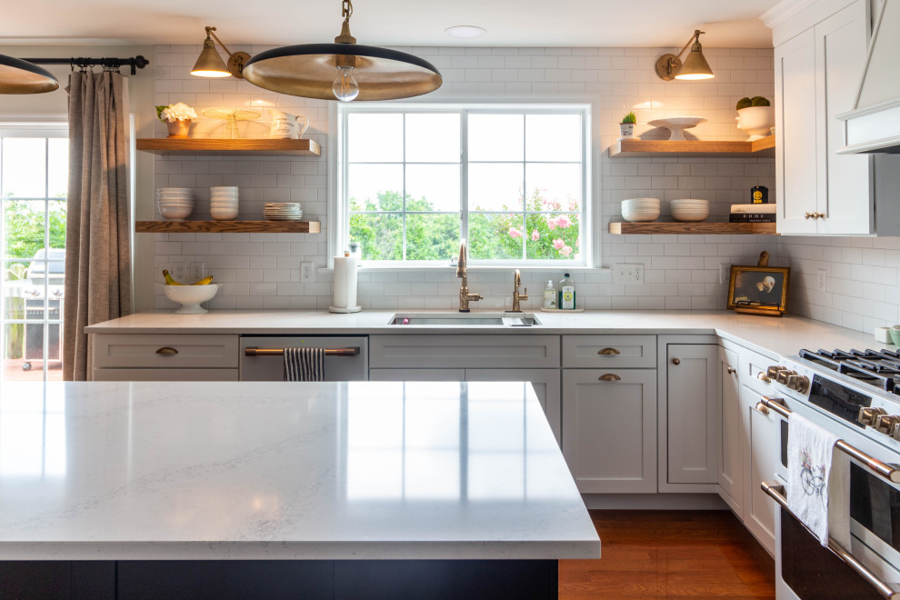 Mid-sized transitional l-shaped medium tone wood floor and brown floor open concept kitchen photo with an undermount sink, shaker cabinets, white cabinets, quartzite countertops, white backsplash, ceramic backsplash, white appliances, an island and white countertops