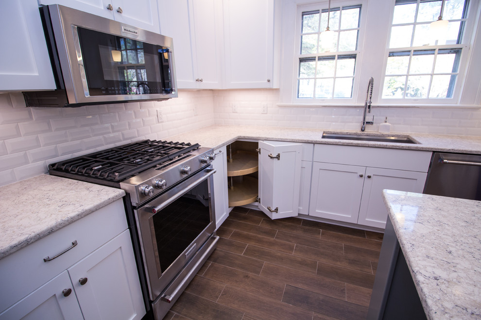 Example of a small u-shaped ceramic tile eat-in kitchen design with an undermount sink, shaker cabinets, white cabinets, quartz countertops, white backsplash, subway tile backsplash, stainless steel appliances, an island and white countertops
