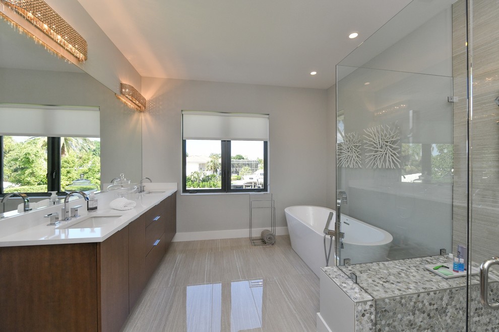 Design ideas for a mid-sized modern master bathroom in Tampa with flat-panel cabinets, dark wood cabinets, a japanese tub, a one-piece toilet, gray tile, grey walls, an undermount sink, a corner shower, a hinged shower door and beige floor.