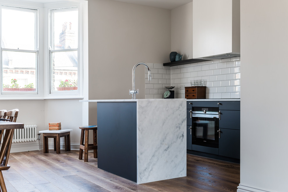 This is an example of a small scandinavian u-shaped open plan kitchen in London with a drop-in sink, recessed-panel cabinets, black cabinets, marble benchtops, white splashback, cement tile splashback, stainless steel appliances, dark hardwood floors and with island.