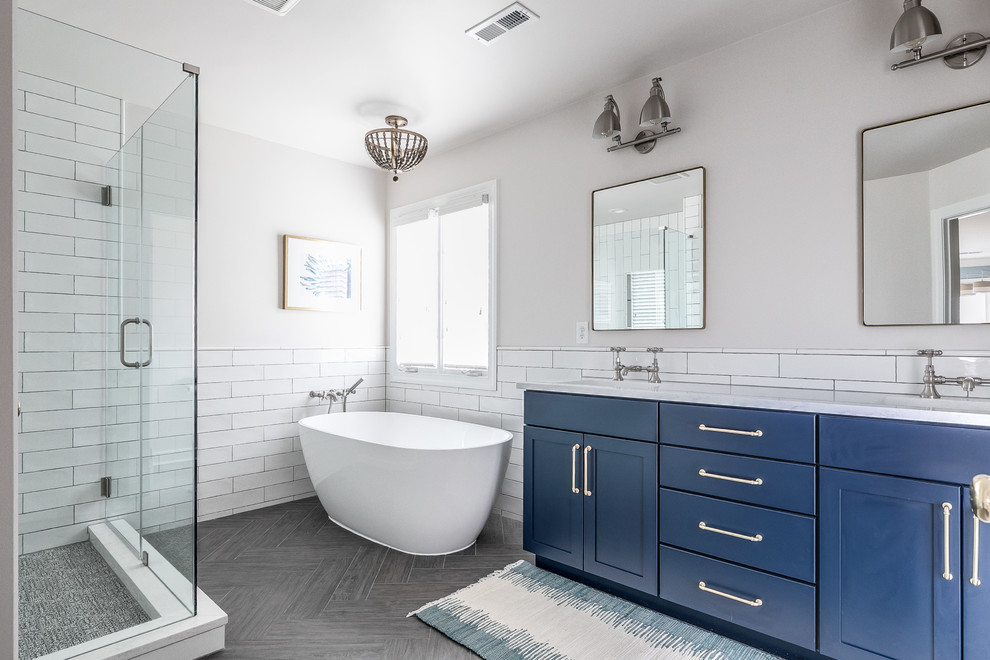 This is an example of a large contemporary master bathroom in Richmond with recessed-panel cabinets, blue cabinets, a freestanding tub, a corner shower, a two-piece toilet, white tile, subway tile, white walls, porcelain floors, an undermount sink, engineered quartz benchtops, grey floor, a hinged shower door and white benchtops.