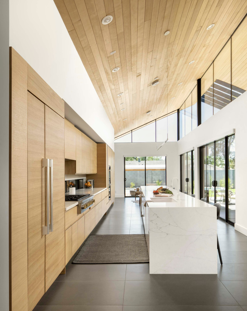 Cette photo montre une cuisine américaine parallèle moderne en bois clair avec un évier posé, un plan de travail en quartz modifié, fenêtre, îlot, un sol gris, un plan de travail blanc et un plafond en bois.