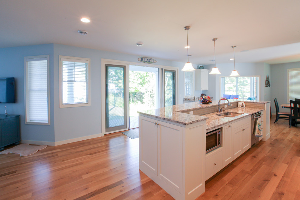 Beach style single-wall open plan kitchen in Grand Rapids with shaker cabinets, white cabinets, granite benchtops, white splashback, porcelain splashback, stainless steel appliances, light hardwood floors and with island.
