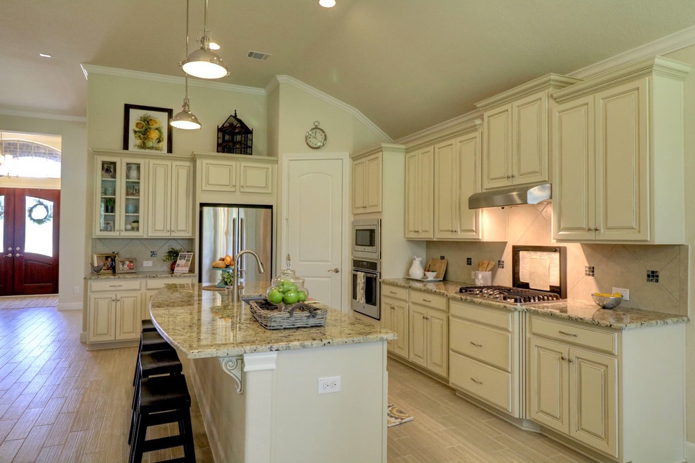 Mid-sized transitional l-shaped open plan kitchen in Houston with an undermount sink, raised-panel cabinets, beige cabinets, granite benchtops, beige splashback, ceramic splashback, stainless steel appliances, porcelain floors, with island and beige floor.