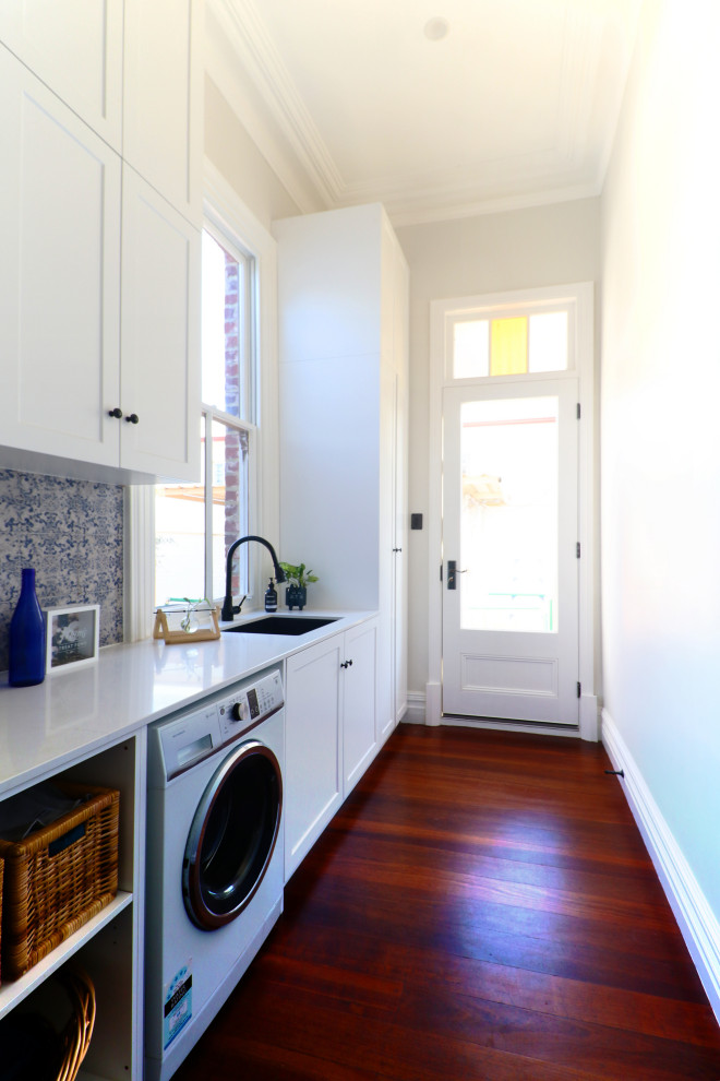 Photo of a mid-sized traditional galley dedicated laundry room in Perth with shaker cabinets, white cabinets, quartz benchtops, blue splashback, ceramic splashback, white walls, dark hardwood floors and yellow benchtop.
