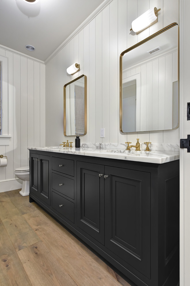 Design ideas for a mid-sized country master bathroom in Charleston with recessed-panel cabinets, black cabinets, white walls, medium hardwood floors, an undermount sink, marble benchtops, brown floor and grey benchtops.