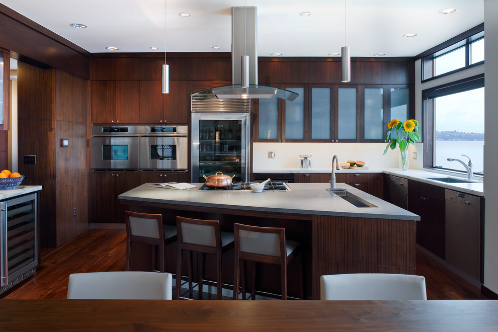 This is an example of a contemporary eat-in kitchen in Seattle with an undermount sink, flat-panel cabinets, dark wood cabinets, white splashback and stainless steel appliances.