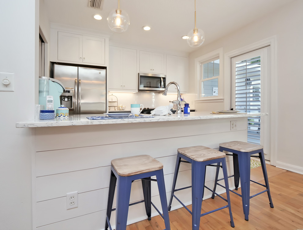 This is an example of a small beach style galley eat-in kitchen in Jacksonville with a farmhouse sink, beaded inset cabinets, blue cabinets, quartz benchtops, white splashback, subway tile splashback, stainless steel appliances, medium hardwood floors, a peninsula, beige floor and white benchtop.