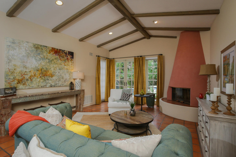 Modelo de sala de estar abovedada mediterránea con paredes beige, suelo de baldosas de terracota, chimenea de esquina, marco de chimenea de yeso, suelo naranja y vigas vistas
