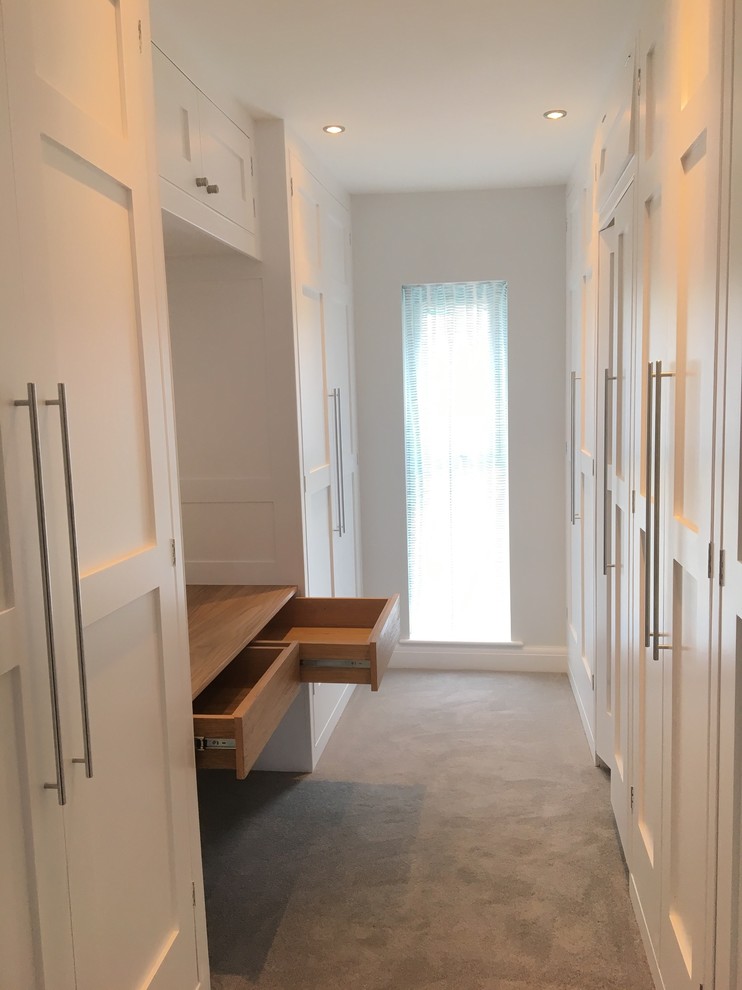 This is an example of a mid-sized transitional gender-neutral walk-in wardrobe in Other with shaker cabinets, white cabinets, carpet and grey floor.