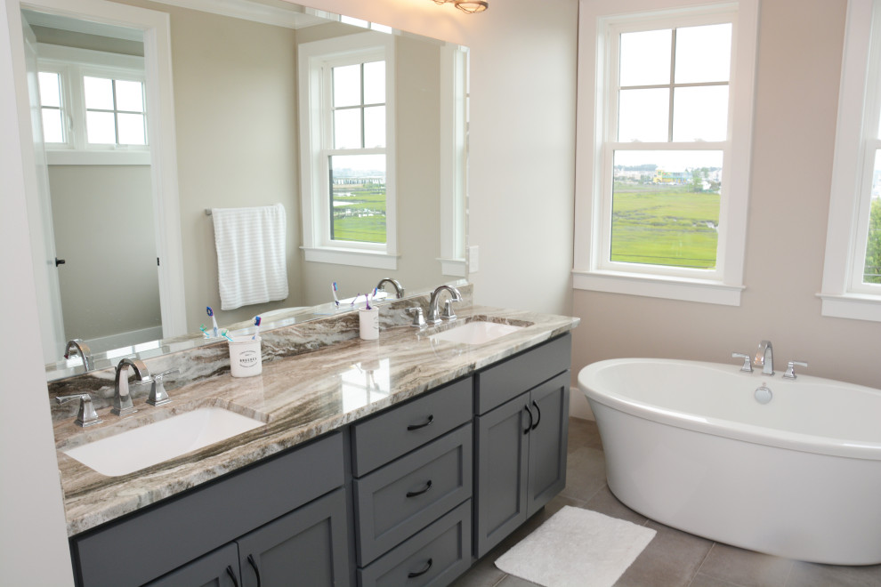 Design ideas for a mid-sized beach style master bathroom in Baltimore with shaker cabinets, grey cabinets, a freestanding tub, beige walls, an undermount sink, granite benchtops, grey floor, beige benchtops, a double vanity and a freestanding vanity.