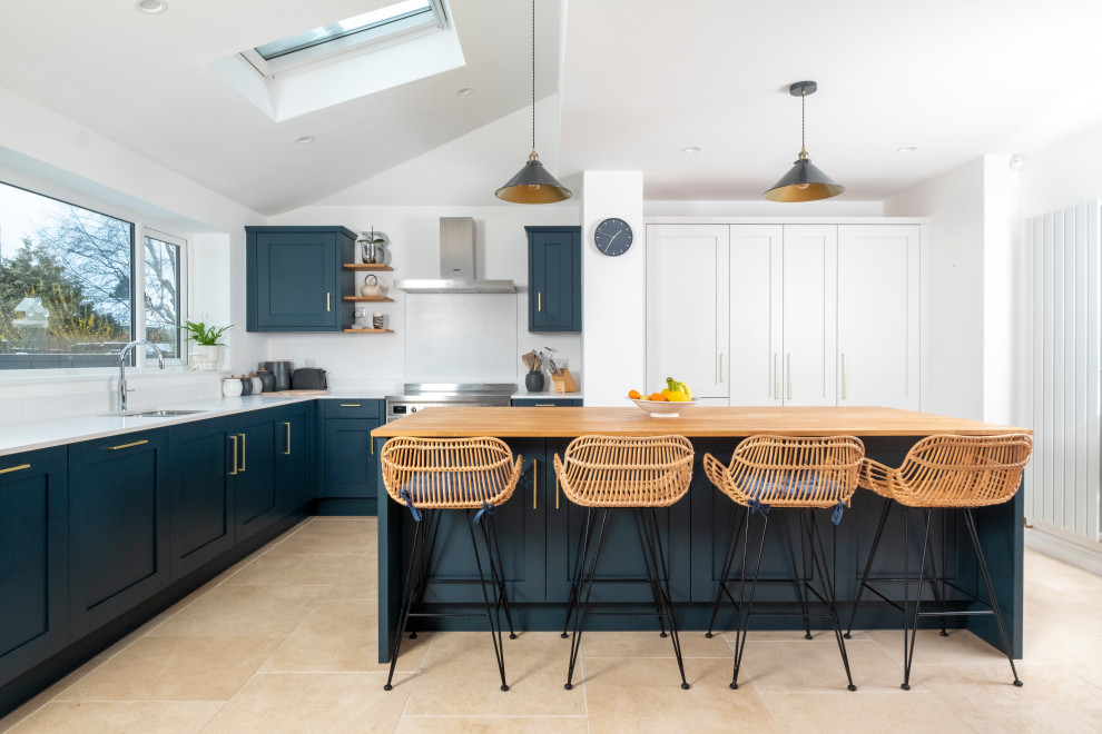Inspiration for a medium sized traditional l-shaped open plan kitchen in Cardiff with shaker cabinets, blue cabinets, composite countertops, glass sheet splashback, stainless steel appliances, porcelain flooring, an island, beige floors, white worktops and a vaulted ceiling.