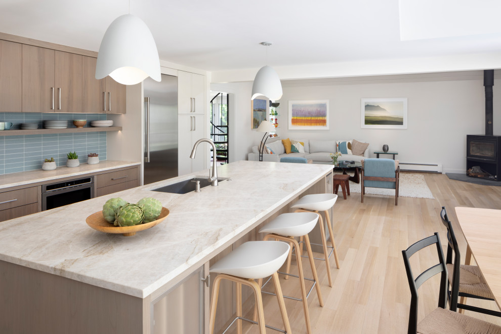 Inspiration for an expansive beach style l-shaped open plan kitchen in New York with an undermount sink, flat-panel cabinets, beige cabinets, marble benchtops, beige splashback, marble splashback, stainless steel appliances, light hardwood floors, with island, beige floor, beige benchtop and vaulted.
