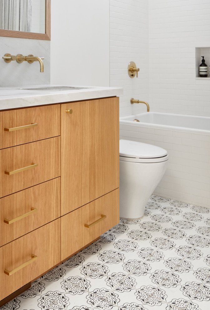 This is an example of a mid-sized scandinavian 3/4 bathroom in San Francisco with flat-panel cabinets, light wood cabinets, an alcove tub, a shower/bathtub combo, white tile, subway tile, white walls, cement tiles, an undermount sink, marble benchtops, multi-coloured floor and grey benchtops.