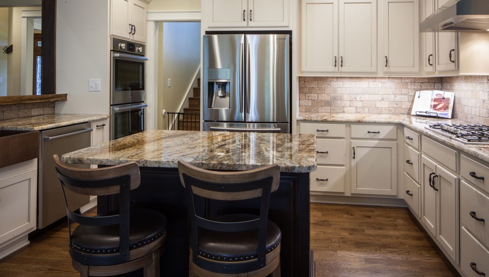 Example of a mid-sized transitional u-shaped dark wood floor and brown floor eat-in kitchen design with a farmhouse sink, recessed-panel cabinets, white cabinets, granite countertops, beige backsplash, ceramic backsplash, stainless steel appliances and an island