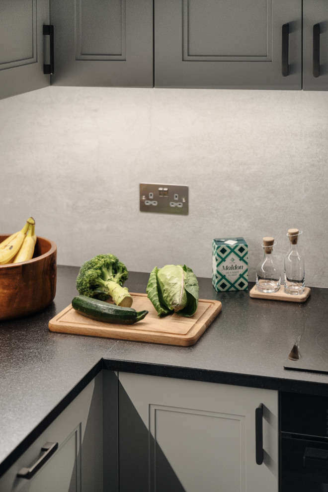 Small eclectic grey and brown l-shaped enclosed kitchen in London with a single-bowl sink, shaker cabinets, grey cabinets, granite worktops, grey splashback, porcelain splashback, black appliances, porcelain flooring, a breakfast bar, multi-coloured floors, black worktops and a drop ceiling.