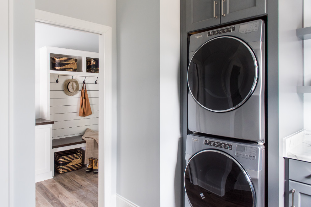 Photo of a mid-sized contemporary l-shaped dedicated laundry room in Indianapolis with an undermount sink, shaker cabinets, grey cabinets, marble benchtops, beige walls, dark hardwood floors and a stacked washer and dryer.