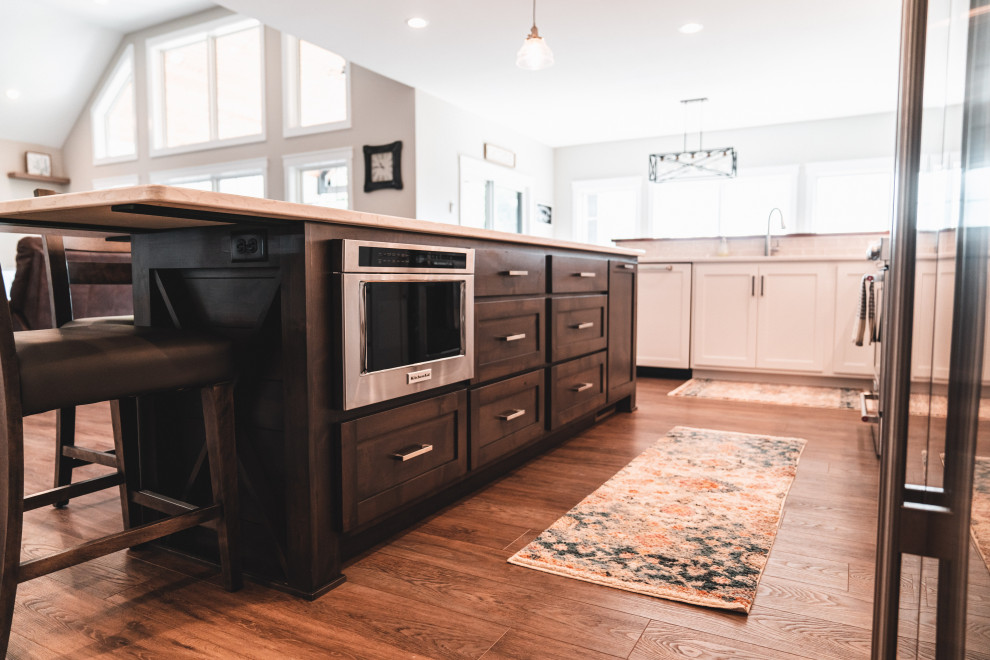 Example of a large transitional l-shaped vinyl floor and brown floor kitchen pantry design with an undermount sink, shaker cabinets, white cabinets, quartz countertops, gray backsplash, subway tile backsplash, stainless steel appliances, an island and white countertops