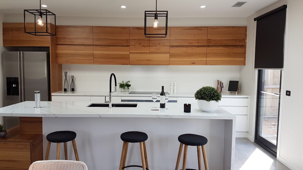 This is an example of a mid-sized contemporary single-wall eat-in kitchen in Geelong with an undermount sink, flat-panel cabinets, medium wood cabinets, quartz benchtops, white splashback, ceramic splashback, stainless steel appliances, terrazzo floors, with island and white floor.