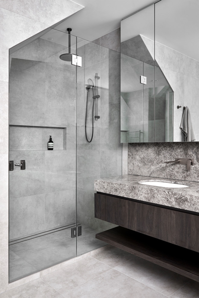 This is an example of a medium sized contemporary ensuite bathroom in Melbourne with dark wood cabinets, a freestanding bath, a one-piece toilet, grey tiles, ceramic tiles, grey walls, ceramic flooring, a submerged sink, limestone worktops, grey floors, a hinged door, grey worktops, a wall niche, double sinks, a built in vanity unit and flat-panel cabinets.