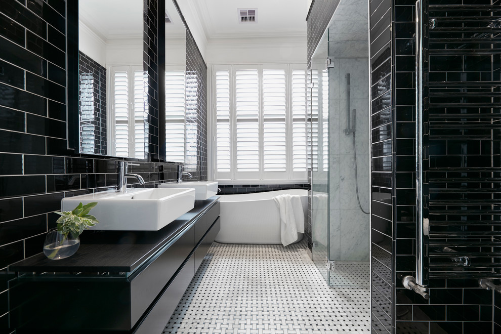 Photo of a contemporary bathroom in Melbourne with flat-panel cabinets, black cabinets, a freestanding tub, a curbless shower, black tile, subway tile, black walls, marble floors, a wall-mount sink and a hinged shower door.